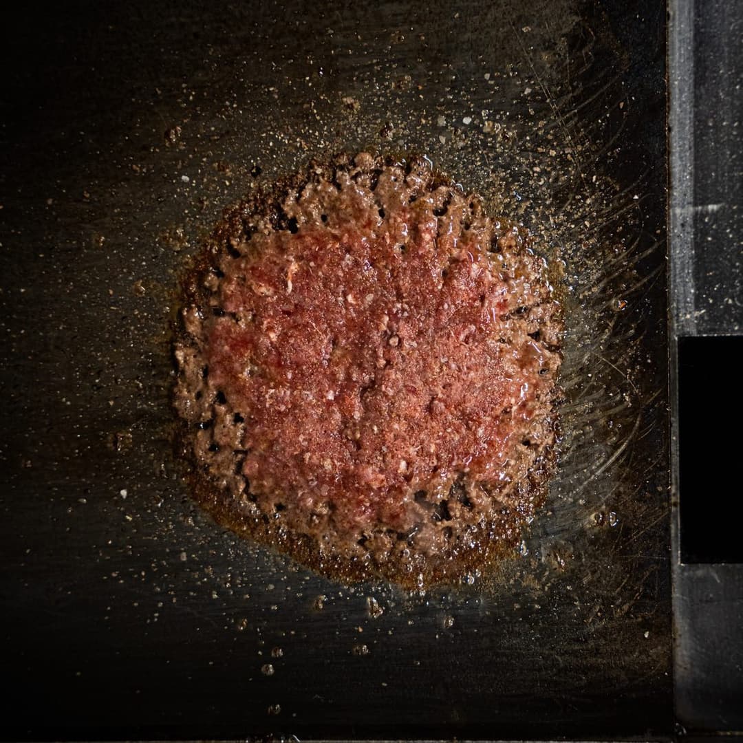Smash burger patty searing on the griddle at Goldies