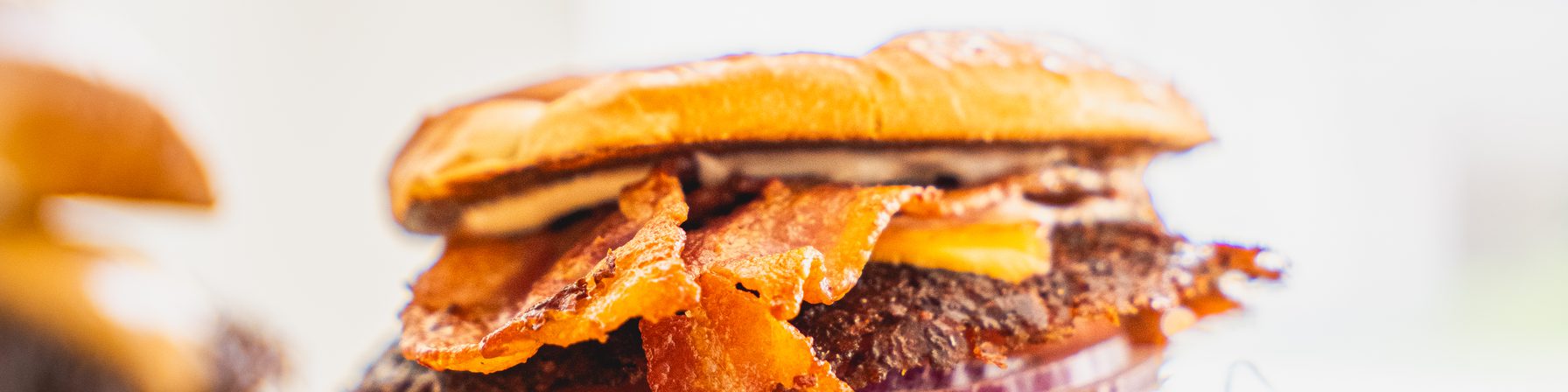 A Goldies smash burger piled with bacon, cheese, red onion and shredded lettuce on a wooden board
